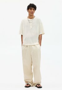 Light beige short-sleeve shirt with a textured finish and button detail, paired with loose-fitting beige pants and black flip-flops.