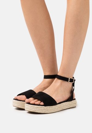 Czarne zamszowe sandały espadryle z paskiem na kostkę, z juty owiniętymi podeszwami, otwartym noskiem i płaskim obcasem. Regulowane metalowe zapięcie.