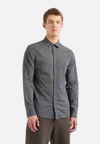 Maglietta a maniche lunghe di colore blu scuro con un sottile motivo geometrico. Presenta un colletto a bottoni e un orlo dritto. Tessuto morbido.