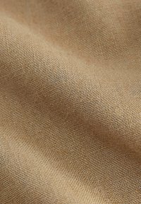 Tissu tissé brun clair avec une texture visible et des plis créant de douces ondulations à travers la surface.