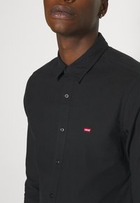 Chemise noire boutonnée en coton, dotée d'un col, de manches longues et d'un petit logo Levi's rouge sur la poitrine.