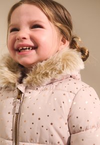 Svjetloružičasta puhasta jakna s uzorcima zlatnih zvijezda i ovratnikom od umjetnog krzna, s prednjim patentnim zatvaračem i podstavom za toplinu.