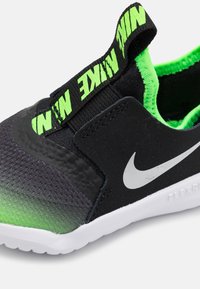 Baskets slip-on noires et vertes avec une finition texturée, présentant un intérieur vert fluo, une sangle noire avec le logo "NIKE" et une semelle blanche.