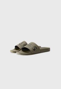 Green slide sandals with a wide rubber strap featuring a raised logo. Textured footbed and flat sole for comfort.