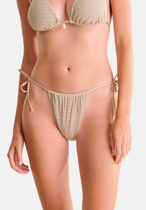 Beige gebreide bikini set met driehoekige top en zijstrik-broekjes, gedragen door een model tegen een effen achtergrond.