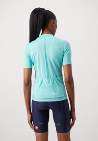 Ein Damen-Radtrikot mit kurzen Ärmeln in Hellblau, mit Belüftung im Rücken, elastischem Saum und Rückentaschen. Kombiniert mit Dunkelblauen Shorts.