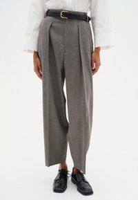Grijze houndstooth broek met plooien, hoge taille en een zwart leren riem met een gouden gesp, gecombineerd met zwarte veterschoenen.