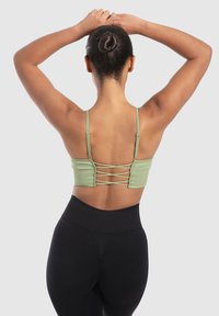 Sujetador deportivo verde con textura de canalé que presenta tirantes cruzados en la parte posterior, complementado con leggins negros de cintura alta. Textura suave, diseño ajustado.