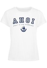 Weißes Baumwoll-T-Shirt mit kurzen Ärmeln. Mit blauer Schrift "AHOI" und einer Grafik von einem Anker und einem Matrosen. Leicht taillierter Schnitt.