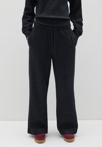 Schwarze weite Sweatpants mit speckled Struktur, elastischem Bund und Kordelzugverschluss. Kombiniert mit roten Schuhen.