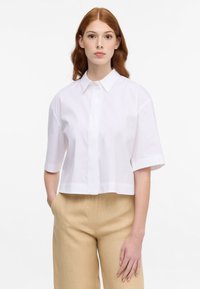 Cropped short-sleeve shirt in white, featuring a classic collar and button closure, made from a smooth, lightweight fabric.