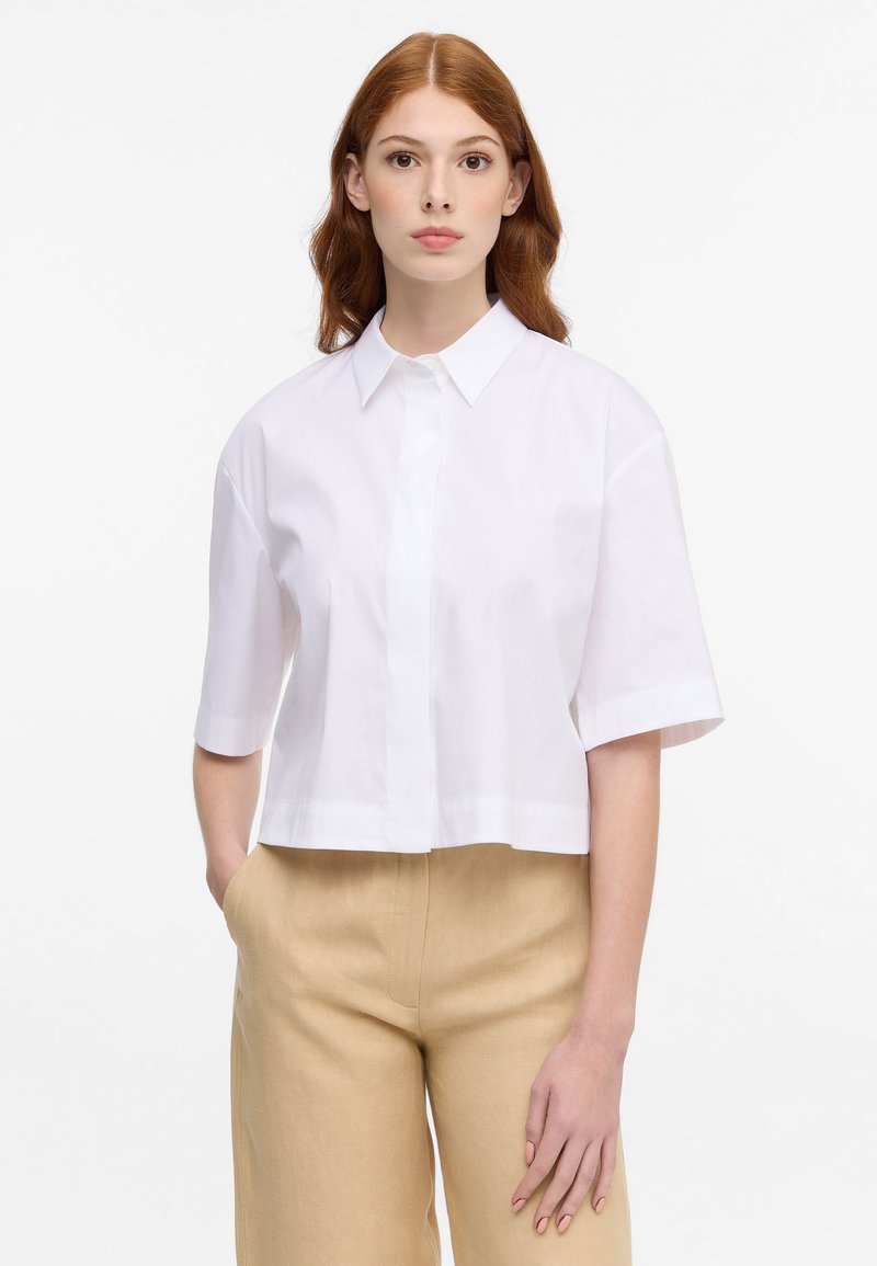 Cropped short-sleeve shirt in white, featuring a classic collar and button closure, made from a smooth, lightweight fabric.