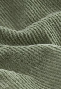 Groene ribstof met een zachte textuur, met verticale lijnen. Het oppervlak heeft een subtiele glans en is iets donzig.