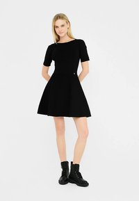 Rochie neagră cu mâneci scurte, cu corset mulat și fustă evazată. Material neted, design minimalist, asortată cu bocanci negri cu sireturi până la gleznă.