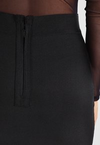 Falda lápiz negra con una tela acanalada texturizada y un cierre discreto en la parte posterior, diseñada para una silueta ajustada.