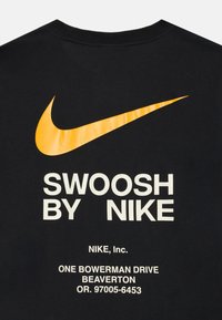Melna auduma ar oranžu Nike švīku un baltu tekstu "Swoosh by Nike" un uzņēmuma adresi zemāk.