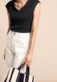 Svart ärmlös topp med V-ringning, i kombination med vita högmidjade jeans. Håller en stor canvasväska med svart och vita ränder.