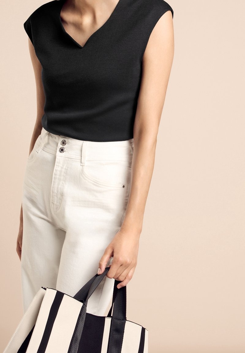 Svart ärmlös topp med V-ringning, i kombination med vita högmidjade jeans. Håller en stor canvasväska med svart och vita ränder.