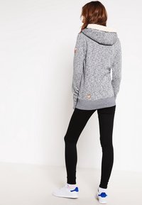 Huppari, jossa on pehmeä kermavärinen vuori hupussa ja ribbireunat. Yhdistetty mustiin legginsseihin ja valkoisiin lenkkareihin, joissa on siniset yksityiskohdat.