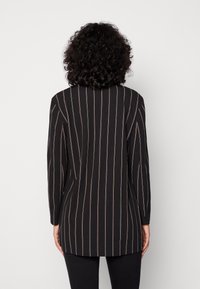 Långärmad svart skjorta med vertikala vita och kopparfärgade ränder. Lättviktigt tyg, kragedesign, och rak bakslut.