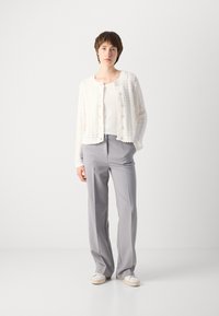 Hvit strikket cardigan med knapper, sammen med en hvit tanktopp og lysegrå vide bukser. Uformelt fottøy fullfører antrekket.