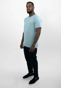 Lichtblauw katoenen T-shirt met een ronde halslijn en korte mouwen, gecombineerd met donkere slim-fit broeken en zwarte instap schoenen.