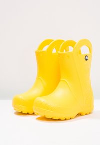 Žluté gumové dešťové boty s kulatou špičkou, otevřenou patou a texturovanou podrážkou. Obsahují logo "crocs" na boku a hladký vnější povrch.