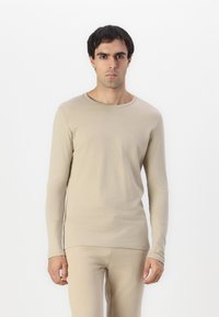 Camisa de manga larga beige hecha de una tela suave con un escote redondo. Diseño ajustado, textura lisa y estilo minimalista, combinada con pantalones a juego.