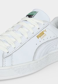 Λευκό sneaker Puma από σουέντ με λευκά κορδόνια, υφασμένο πάτο, χρυσό λογότυπο Puma και πράσινη ετικέτα Puma στη γλώσσα.