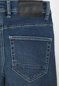 Hintertasche einer blauen Denim-Jeans mit kontrastierenden weißen Nähten und einem schwarzen Lederlabel am Taillenbund.