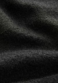 Dunkel strukturiertem Stoff mit einer flauschigen Oberfläche, der eine tiefschwarze Farbe und ein unregelmäßiges Webmuster zeigt, was Wärme und Dicke suggeriert.