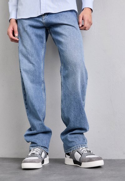 Jeans din denim de culoare albastru deschis, cu o croială dreaptă, având o ușoară decolorare. Asortați cu adidași gri și albi și o cămașă căptușită cu dungi albastre deschise.