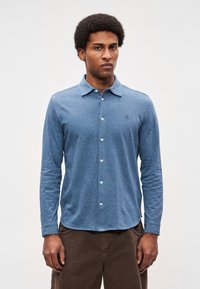 Polo azul de mangas compridas em tecido texturizado, com fecho frontal de botões e pequeno logótipo bordado no peito.