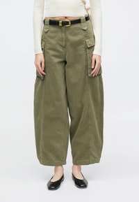 Pantaloni cargo verde măsliniu cu croială lejeră, prevăzuți cu multiple buzunare, o curea cu cataramă aurie și un material moale din bumbac.