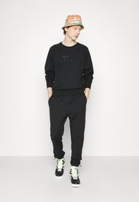 Mustmust ja dressipüksid, millel on silmatorkav Nike logo. Mustritega mitmevärviline kübar. Mustad ja rohelised kõrgemad tennisetossud.