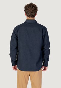 Chemise boutonnière bleu marine à manches longues et col, fabriquée dans un tissu texturé avec un ourlet incurvé.