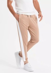 Beige joggers met witte zijkanten, voorzien van twee zakken en een tailleband met trekkoord. Draag je met witte sneakers. Gladde stoftextuur.