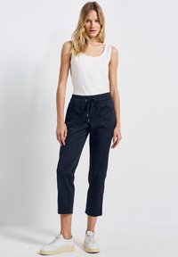 Pantalones cortos azul marino con cintura elástica y cordón, que cuentan con bolsillos laterales. El conjunto se complementa con una camiseta sin mangas blanca y zapatillas blancas.