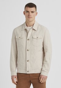 Helle beigefarbene Leinenjacke mit einer Knopfleiste auf der Vorderseite, zwei Brusttaschen und einem klassischen Kragen. Sie besitzt einen strukturierten Stoff und Knopfdetails.