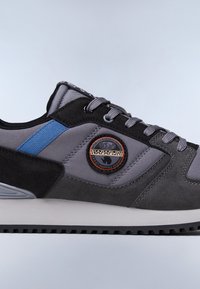 Szare buty sportowe z mieszanką zamszu i materiałów tekstylnych, z niebieskim akcentem w postaci paska oraz widoczną okrągłą łatą z logo. Guma podeszwy.