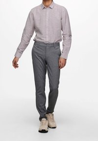 Camisa abotonada de un gris claro con mangas largas, combinada con pantalones oscuros grises y zapatillas beige, creando un atuendo coordinado.