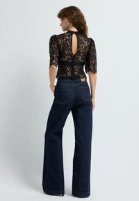 Blusa in pizzo nero con maniche a tre quarti e schiena a chiave, abbinata a jeans a vita alta blu scuro con gambe larghe e tasche posteriori.