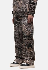 Camo patterned sweatpants in shades of brown and black. Loose fit with elastic waistband and cuffs. Paired with black and white sneakers.