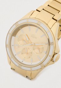 Gold wristwatch with metal band, white and gold bezel marked in increments of 10, and three subdials displaying day, 24-hour, and date functions.