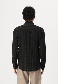 Camisa de cuadros negra y verde oscuro con rayas verticales, mangas largas, puños abotonados y cuello clásico. Tejido texturizado y ligeramente transparente.