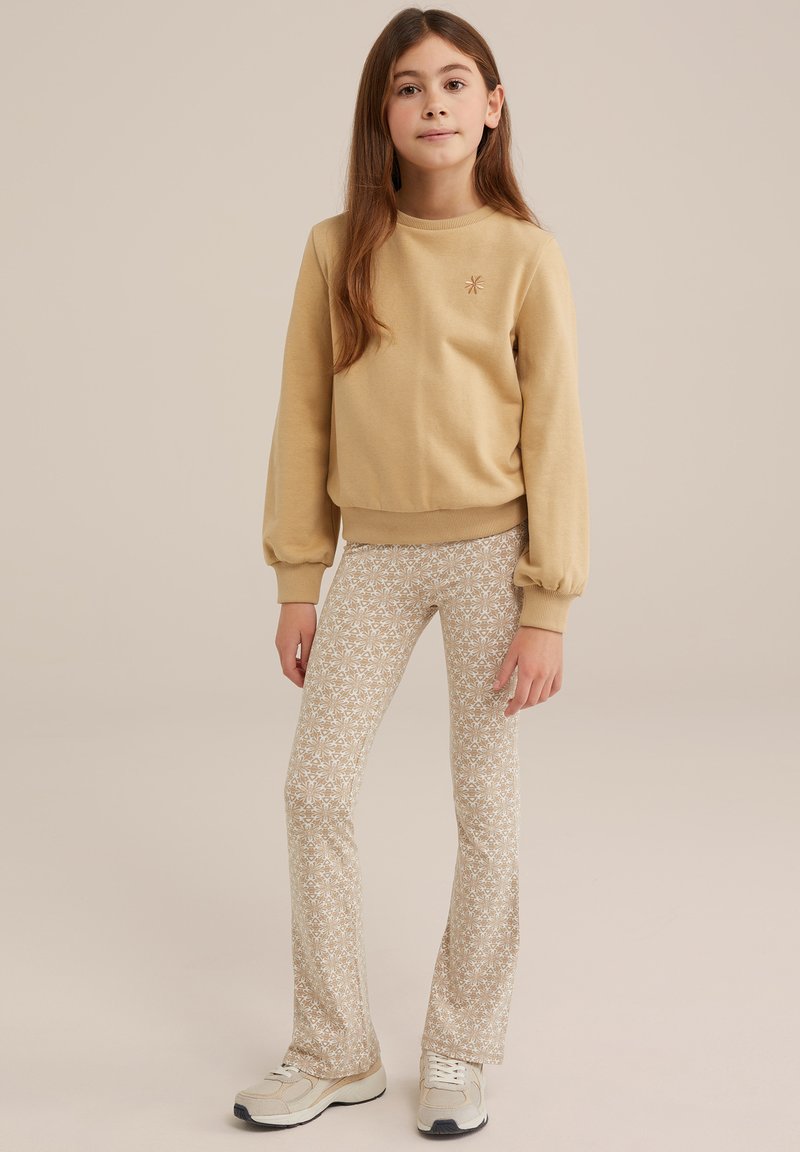 Bež majica s rebrastim manžetami in ovratnikom; patterned bež flare hlače z belimi cvetovi; svetli športni copati z sivo in smetany akcenti.