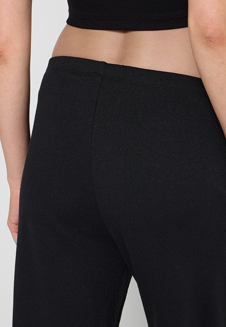 Primer plano de una persona que lleva pantalones negros de cintura alta y una camiseta negra corta, mostrando su parte baja de la espalda y área de la cintura.