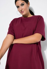 Camiseta oversize burdeos de mangas cortas, hecha de una tela suave, con cuello redondo y ajuste relajado. Textura suave, sin patrones.