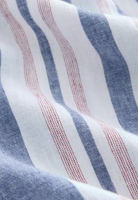 Gestreifter Stoff in Weiß, Blau und Rot. Das Material ist leicht und strukturiert und zeigt abwechselnd breite und schmale Streifen mit einem Gewebemuster.