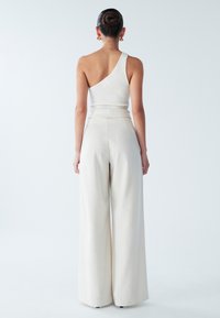 Asymmetrisches weißes Ripp-Top kombiniert mit weit geschnittenen, cremefarbenen Hosen; glatte Textur mit hoher Taille und minimalistischem Design.